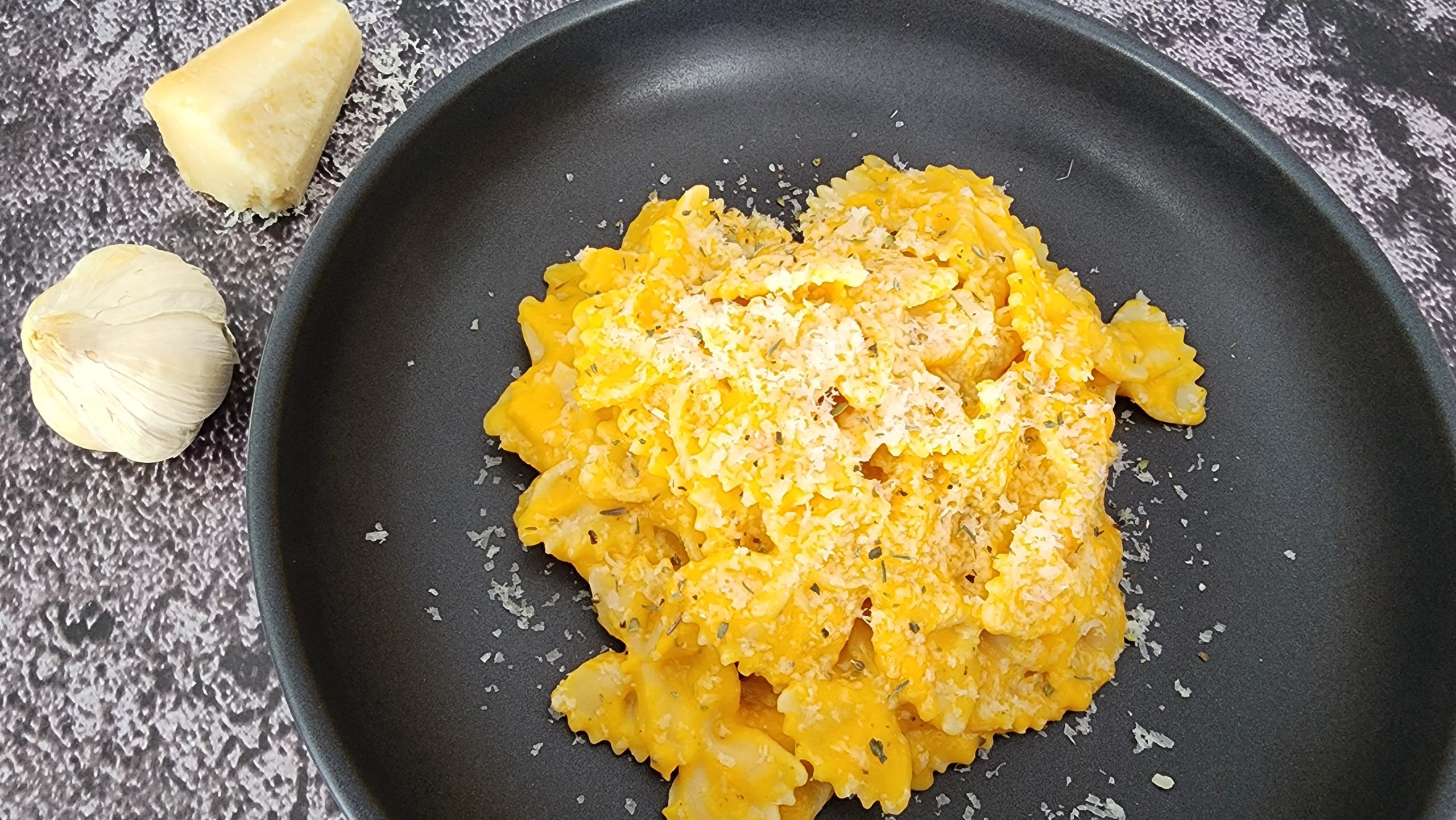 des pâtes farfalles de couleur orangée (car la sauce est à base de courge) dans une assiette noire